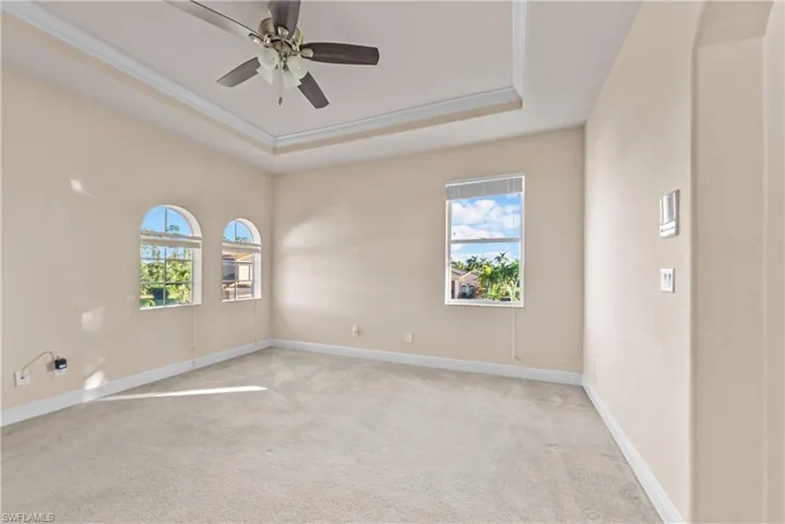 Carpeted empty room featuring a tray ceiling, ceiling fan, and ornamental molding