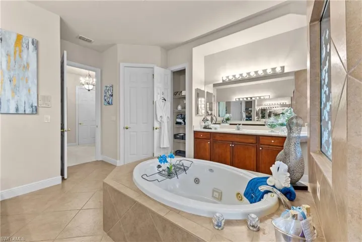 Bathroom with tiled bath, tile patterned flooring, vanity, and an inviting chandelier