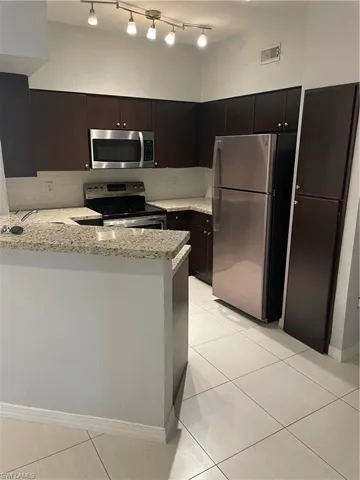 Kitchen featuring range, light tile patterned floors, fridge, a peninsula, and light stone countertops