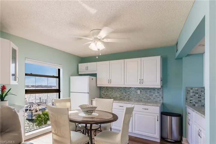Kitchen with white cabinetry, white refrigerator, light wood-type flooring, light stone countertops, and decorative backsplash