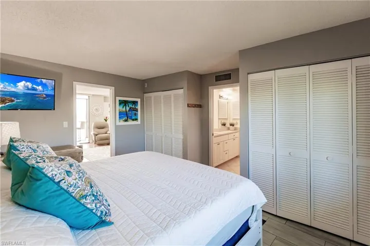 Bedroom with multiple closets, ensuite bath, a textured ceiling, and light wood-type flooring