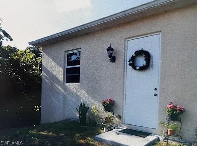 Stucco exterior featuring a white paneled door, single-pane window, and wall-mounted exterior light fixture