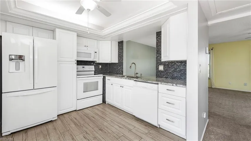 Kitchen featuring white appliances, ceiling fan, white cabinets, backsplash, and light stone counters