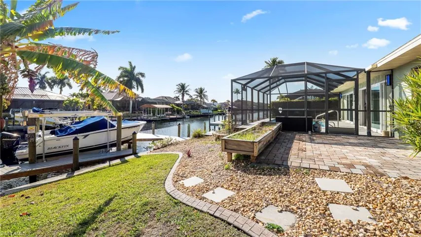 View of green lawn with glass enclosure, a sunroom, a boat dock, a water view, and a patio area