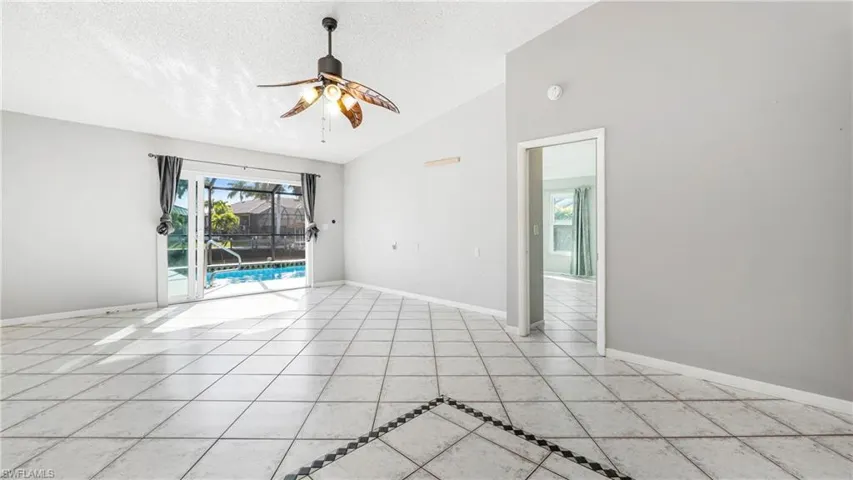 Empty room with a ceiling fan, a high textured ceiling, a sunroom, and light tile patterned floors