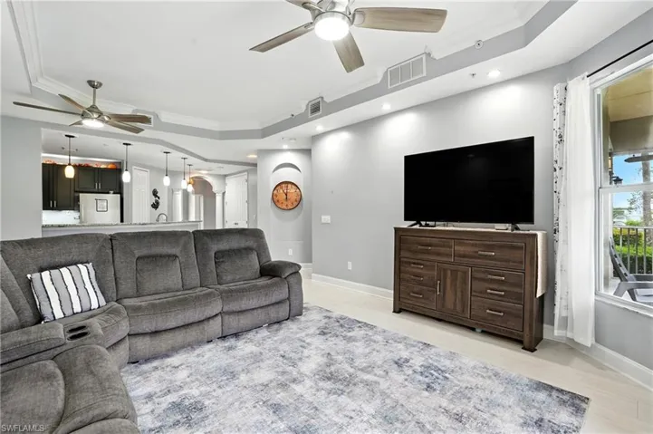 Living area with ornamental molding, a raised ceiling, arched walkways, ceiling fan, and light wood finished floors