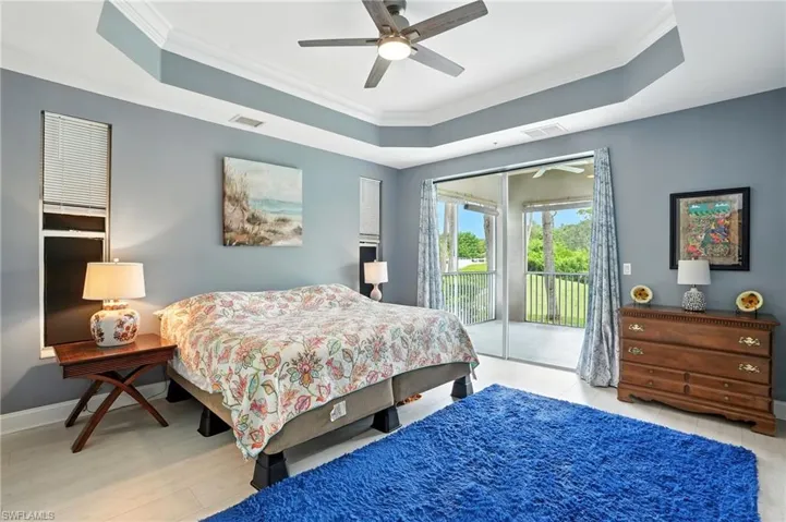 Bedroom with a tray ceiling, ornamental molding, light wood-style flooring, and access to exterior