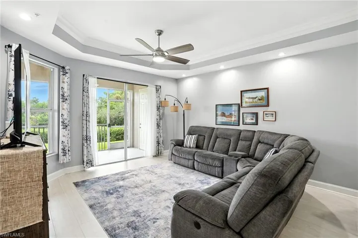 Living room with crown molding, ceiling fan, a raised ceiling, light wood-style floors, and recessed lighting
