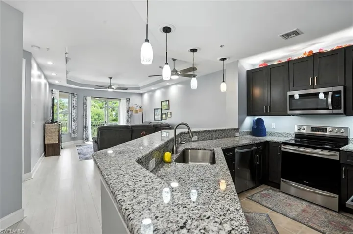 Kitchen featuring appliances with stainless steel finishes, a tray ceiling, light stone counters, hanging light fixtures, and open floor plan