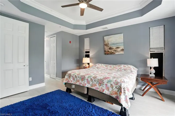 Bedroom featuring a tray ceiling, ornamental molding, light wood-type flooring, and a ceiling fan