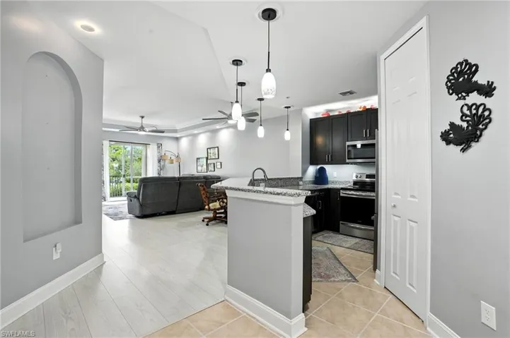 Kitchen with dark cabinets, pendant lighting, stainless steel appliances, light stone countertops, and open floor plan
