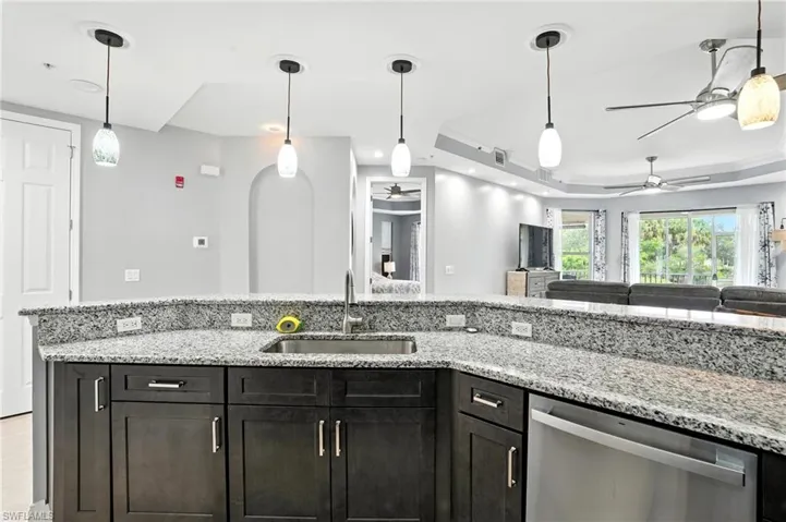 Kitchen featuring a raised ceiling, light stone counters, pendant lighting, and dishwasher