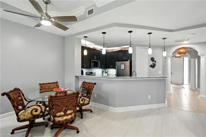 Kitchen featuring arched walkways, decorative columns, dark cabinets, refrigerator, and light wood-type flooring