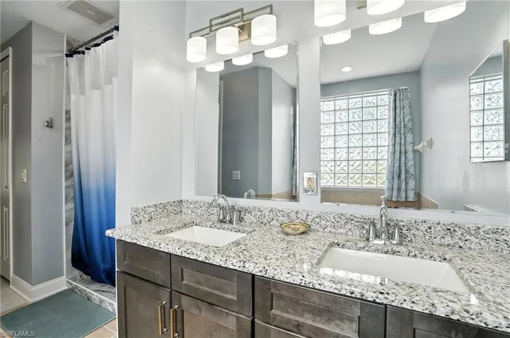 Full bath featuring healthy amount of natural light, double vanity, and a shower stall