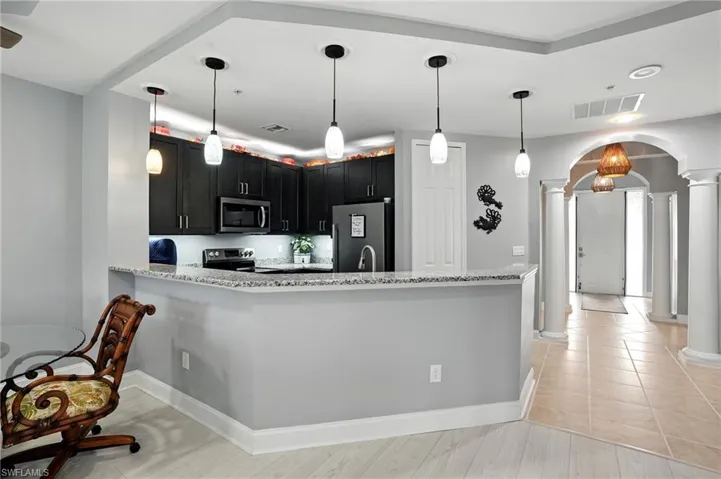 Kitchen featuring decorative columns, arched walkways, pendant lighting, a peninsula, and appliances with stainless steel finishes
