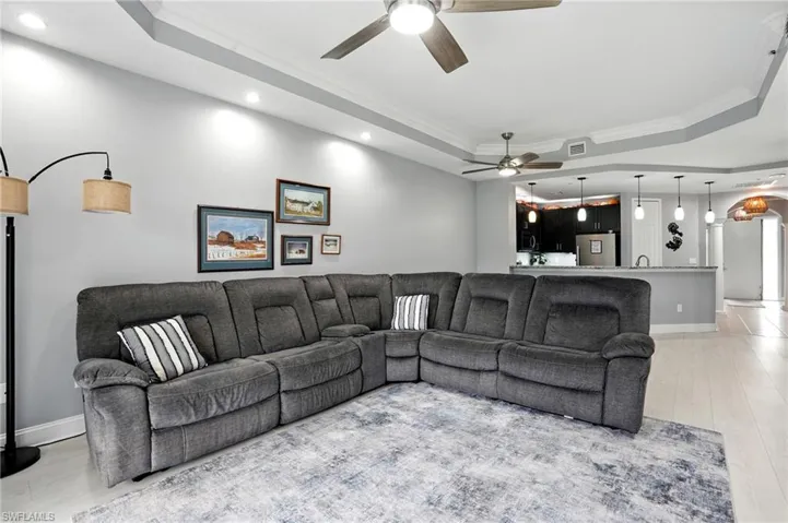 Living area with a tray ceiling, ornamental molding, light wood finished floors, recessed lighting, and a ceiling fan