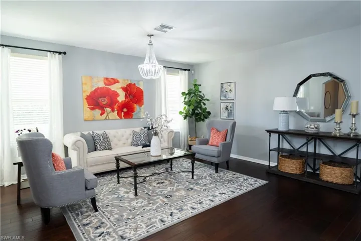 Open-concept living space featuring rich wood-finish flooring, a contemporary chandelier, ample natural light from multiple windows, and a built-in console table with shelving