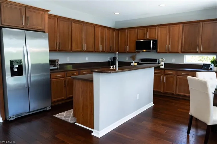 Kitchen featuring rich wood-finish flooring, ample cabinetry with brushed nickel hardware, dark countertops, a stainless steel refrigerator, and recessed lighting