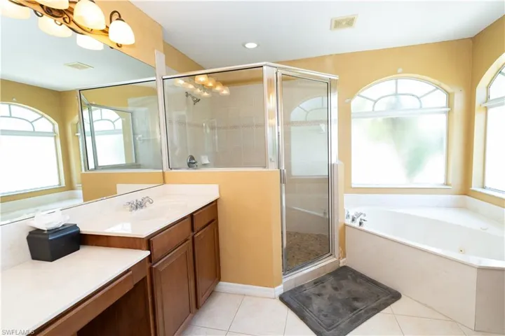 Bathroom featuring a corner soaking tub, a separate glass-enclosed shower, a double vanity with an integrated sink, and arched windows