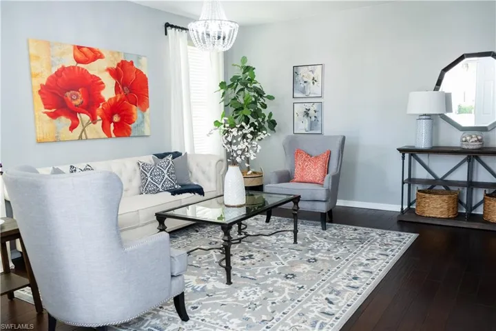 Spacious living area featuring dark wood-finish flooring, a contemporary chandelier, and light-toned walls