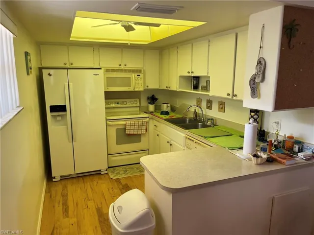 Kitchen featuring white appliances, light countertops, light wood finished floors, a peninsula, and a ceiling fan