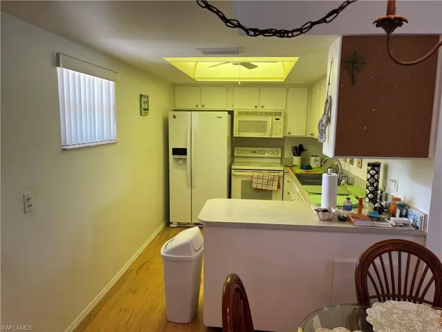 Kitchen with white appliances, light countertops, light wood finished floors, and a peninsula