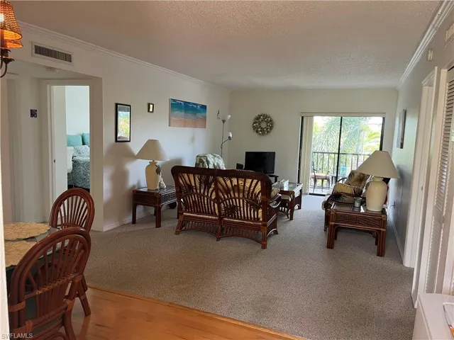 Living room featuring a textured ceiling, ornamental molding, light wood-type flooring, and light colored carpet