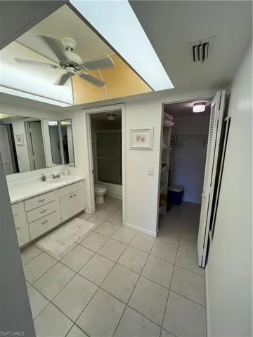 Full bath with vanity, a ceiling fan, light tile patterned floors, and a walk in closet