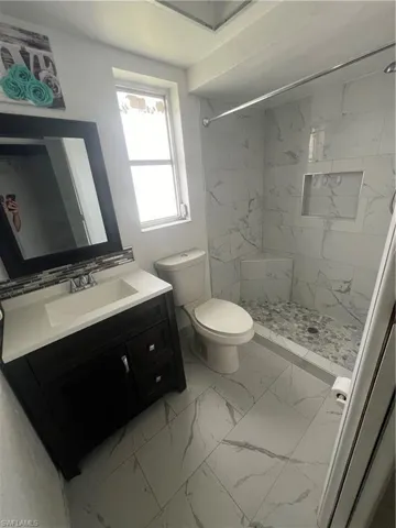 Bathroom with vanity, a tile shower, tile patterned flooring, and toilet