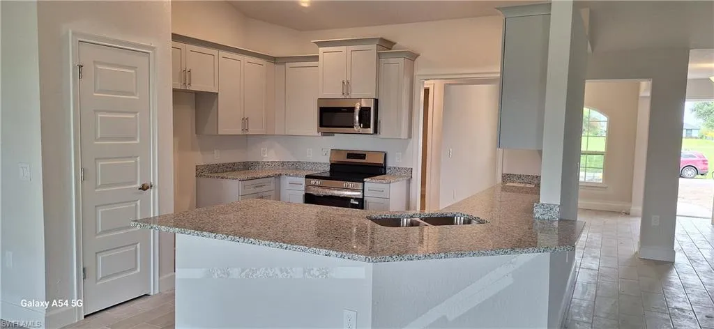 Kitchen featuring stainless steel appliances, a peninsula, light stone counters, wood finish floors, and pendant lighting