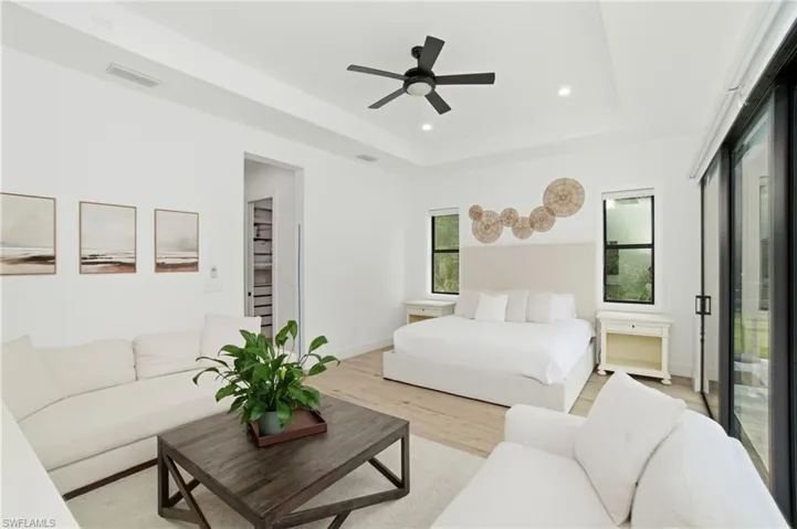Spacious bedroom featuring wood-finish flooring, a tray ceiling with a ceiling fan, recessed lighting, and large sliding glass doors