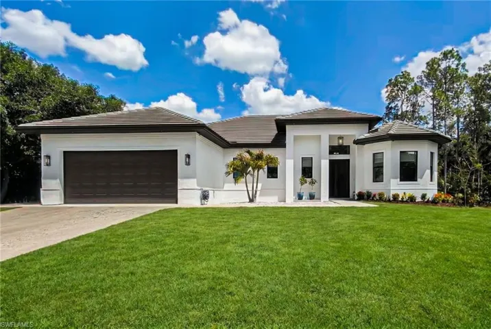 Contemporary stucco exterior with a dark tile roof, an integrated two-car garage, manicured front lawn, and surrounding natural landscaping