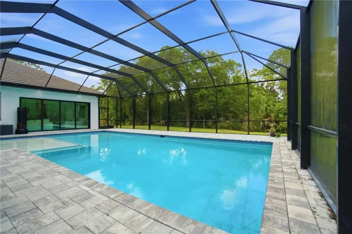 Screened pool enclosure featuring a rectangular pool, integrated spa, and paver decking