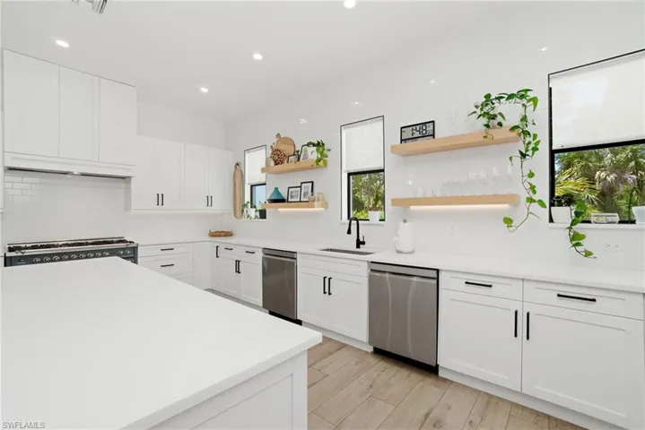 Spacious kitchen featuring white cabinetry, light countertops, subway tile backsplash, stainless steel appliances, and wood-finish flooring