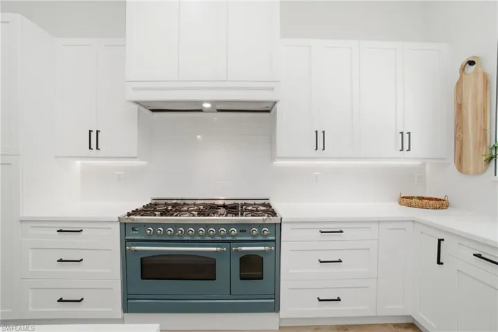 Gourmet kitchen featuring a striking teal range, white shaker-style cabinetry, white countertops, a white subway tile backsplash, and dark hardware