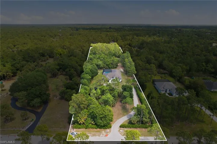 Aerial view showcasing a substantial parcel of land, featuring mature trees and a main residence with a light-colored roof