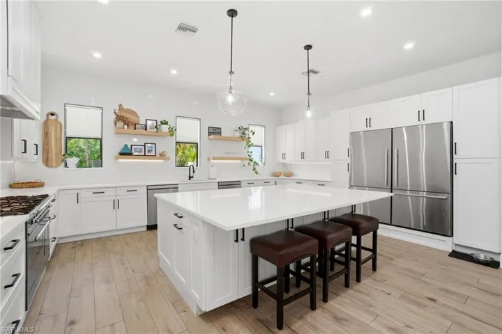 Spacious kitchen featuring an expansive central island with seating, white shaker cabinetry, stainless steel appliances, and light wood-finish flooring