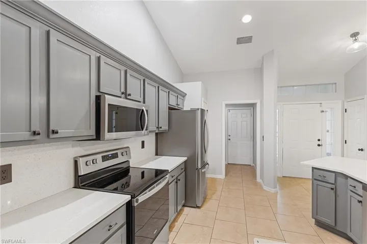 Kitchen with appliances with stainless steel finishes, vaulted ceiling, gray cabinets, decorative backsplash, and light tile patterned floors