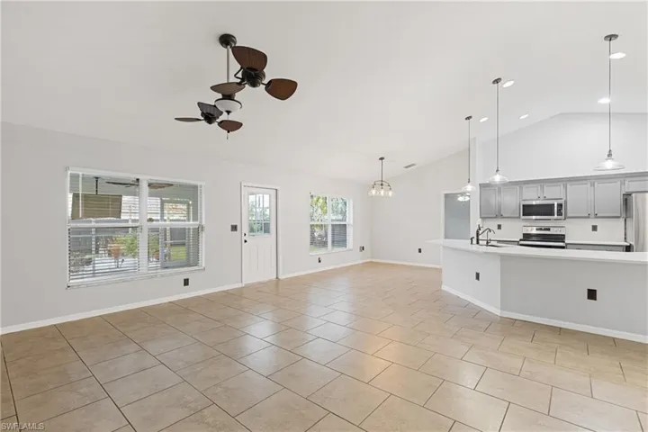 Unfurnished living room featuring light tile patterned flooring, sink, ceiling fan with notable chandelier, and vaulted ceiling