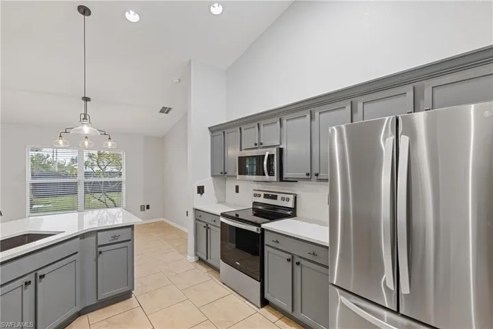 Kitchen with appliances with stainless steel finishes, lofted ceiling, and gray cabinets
