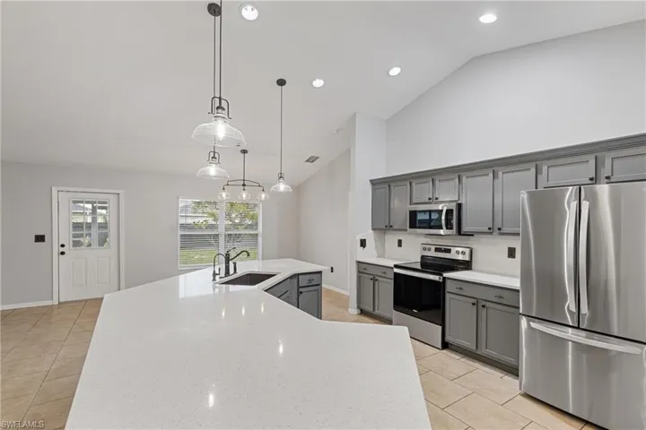 Kitchen with lofted ceiling, stainless steel appliances, sink, gray cabinetry, and decorative light fixtures