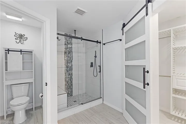 Bathroom with a shower with shower door, hardwood / wood-style flooring, and toilet