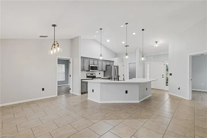 Kitchen with hanging light fixtures, gray cabinetry, stainless steel appliances, a center island with sink, and high vaulted ceiling