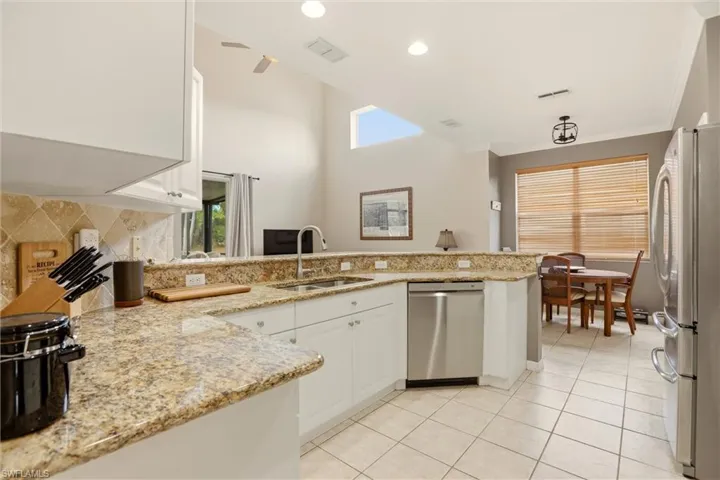 Kitchen featuring light stone counters, a peninsula, white cabinets, recessed lighting, and a high ceiling