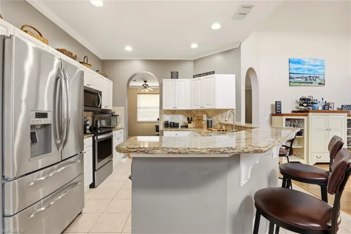 Kitchen with stainless steel appliances, light stone countertops, decorative backsplash, a kitchen breakfast bar, and a ceiling fan