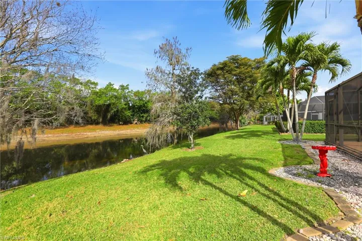 View of grassy yard with a sunroom, a water view, and glass enclosure