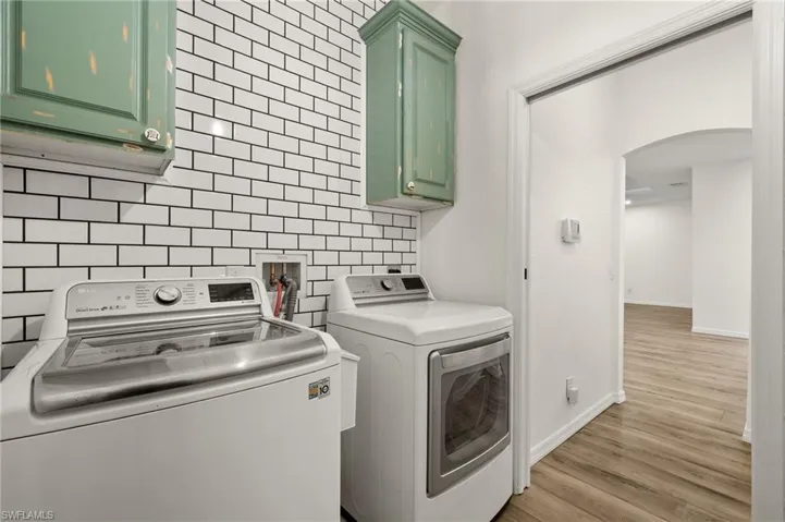 Laundry room with tile walls, light hardwood / wood-style floors, cabinets, and independent washer and dryer