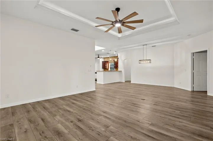 Unfurnished living room featuring wood-type flooring, ceiling fan, and a raised ceiling