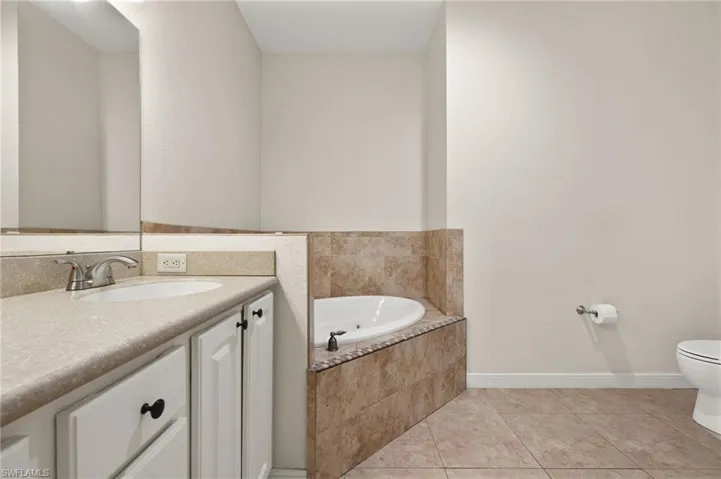 Bathroom featuring toilet, vanity, tile patterned floors, and tiled tub
