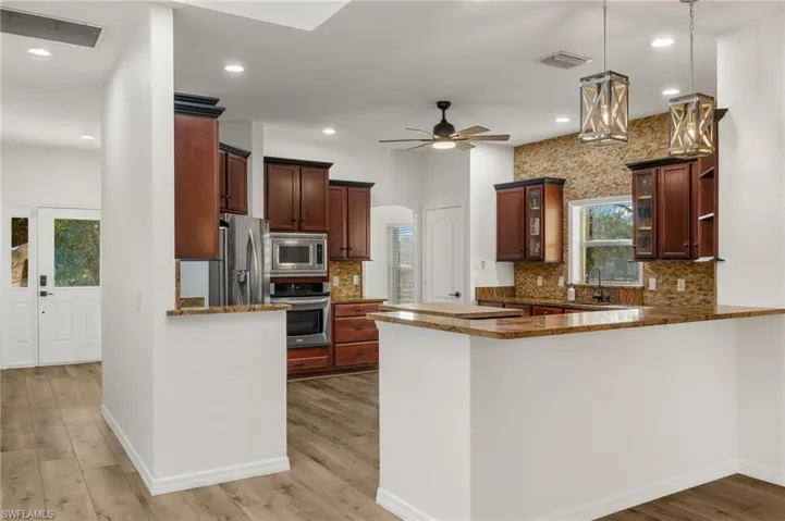Kitchen with stainless steel appliances, light hardwood / wood-style floors, kitchen peninsula, ceiling fan, and decorative light fixtures